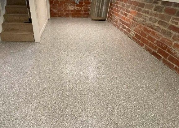 Basement with a gray flake epoxy floor, red brick walls and carpeted stairs