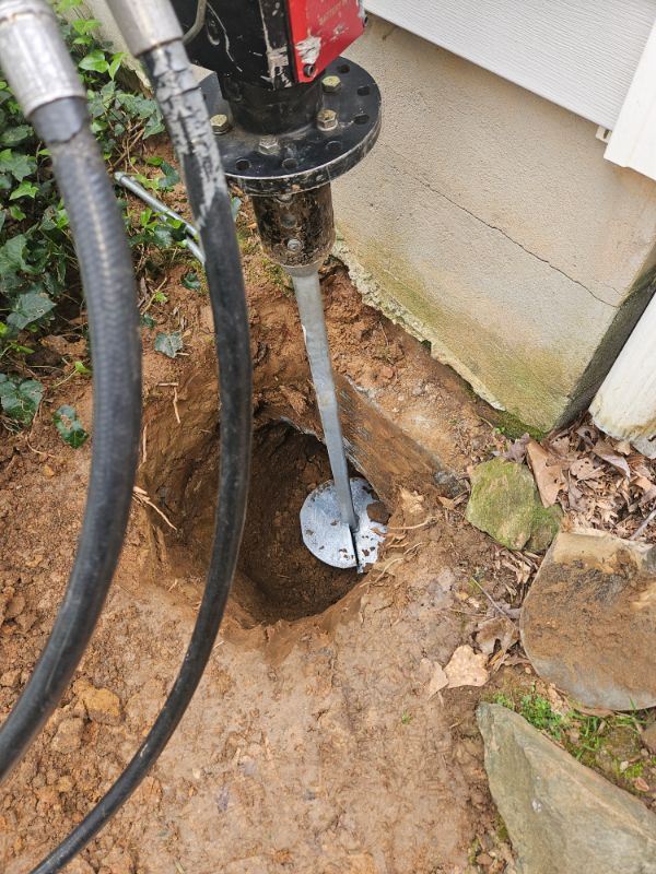 Helical pier being installed with a hydraulic drive head beside a home's foundation